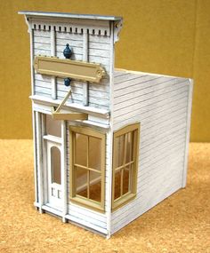 a small white doll house with windows and a clock on the top floor, sitting on a table