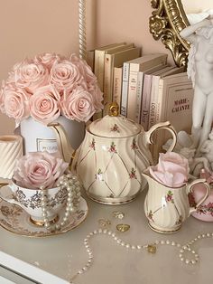 pink roses are in vases and other items on a white table with gold accents