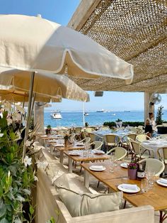 an outdoor dining area with tables, chairs and umbrellas overlooking the ocean on a sunny day