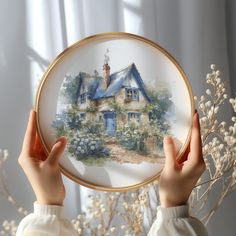 a woman holding up a painting in front of her face, with the image of a house painted on it