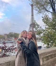 two women standing next to each other in front of the eiffel tower