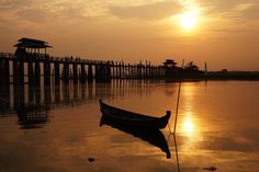 a small boat floating on top of a body of water at sunset in front of a pier