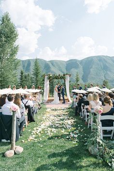 a wedding ceremony in the mountains with white flowers and greenery on the aisle, surrounded by lawn chairs