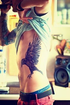 a man with a bird tattoo on his back holding a beer in his right hand