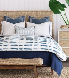 a bed with blue and white pillows on top of it next to a plant in a vase