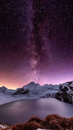 the night sky is filled with stars above a mountain range and a lake in the foreground