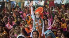 a man in an orange turban and headdress stands among a group of people