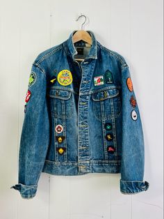 a denim jacket with patches on it hanging from a hanger in front of a white wall