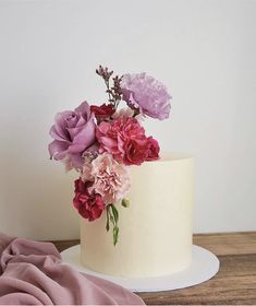 a white cake with pink and red flowers on top, sitting on a wooden table