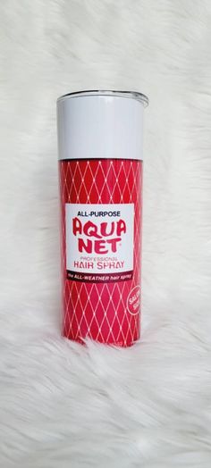 a can of hair spray sitting on top of a white fur covered floor next to a cup