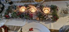 the table is set for christmas dinner with candles and pine cones on it, surrounded by other holiday decorations