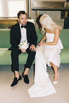 a man in a tuxedo and woman in a wedding dress sitting on a bench