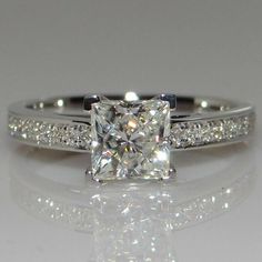 a white gold ring with a princess cut diamond and pave set diamonds on the sides