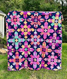 a quilt is hanging on the side of a house in front of some trees and grass