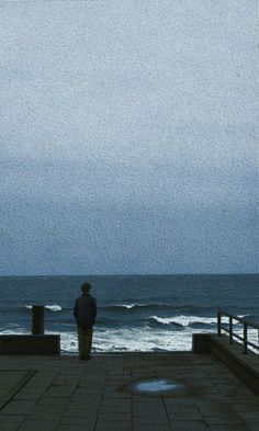 a man standing on the edge of a pier looking out at the ocean in the rain