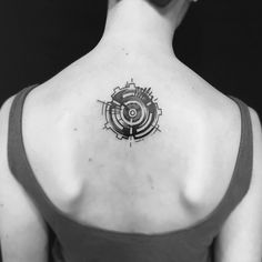 the back of a woman's neck with a circular tattoo on her left shoulder