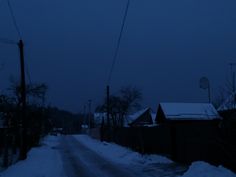 a dark street with snow on the ground and power lines in the distance at night