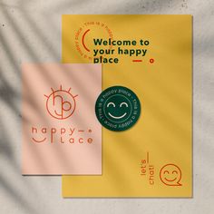 two different logos for happy place on yellow and pink paper