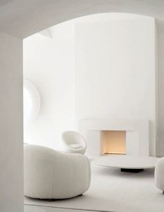 a living room filled with white furniture and a fire place in the middle of it