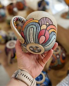 a hand holding a ceramic teapot with flowers painted on it