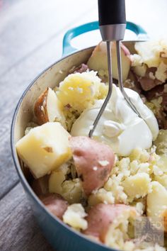 a pot filled with potatoes and meat next to a whisk on top of it