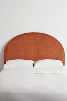 a bed with an orange headboard and white linens on the bottom, against a wall