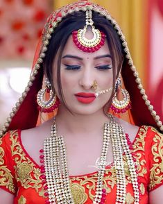 a woman in a red and gold bridal outfit with jewelry on her face, looking at the camera