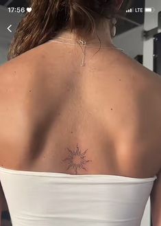 the back of a woman's white top with a sun tattoo on her left shoulder