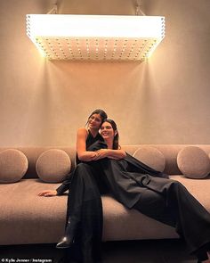 two women are sitting on a couch in front of a light that is above them