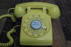 an old yellow telephone sitting on top of a wooden table next to a phone cord