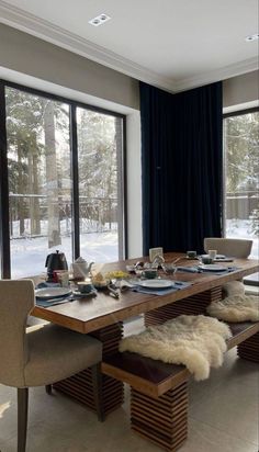 a dining room table is set with place settings and chairs, along with two large windows that look out onto the snow covered yard