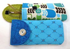 three purses are lined up on a white surface, one is green and the other is blue