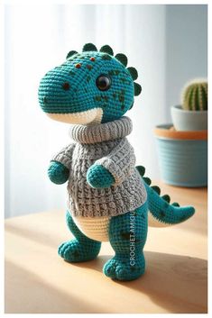 a crocheted dinosaur with a sweater on it's back sitting on a table