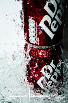 a close up of two cans of soda in water with splashing on the surface