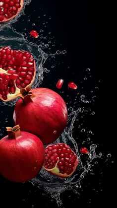 three pomegranates with water splashing around them on a black background