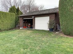 a garage with a lawn and two chairs in front of it, surrounded by hedges