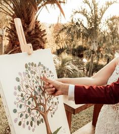 the bride and groom are holding their hands near an easel with a tree on it