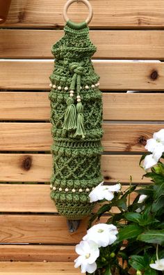 a green crocheted bag hanging on a wooden wall next to flowers and potted plants