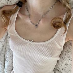 a woman laying on top of a bed wearing a white tank top and black bow tie necklace