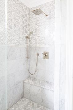 a bathroom with white marble walls and flooring, including a shower head and hand shower