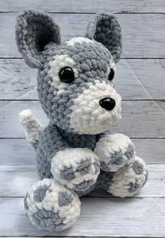 a crocheted gray and white dog sitting on top of a wooden floor next to a wall