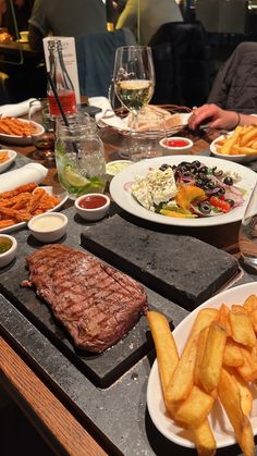 a table full of food including steak, fries and wine