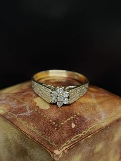 a gold ring with two diamonds on top of an old leather cushioned box in front of a black background