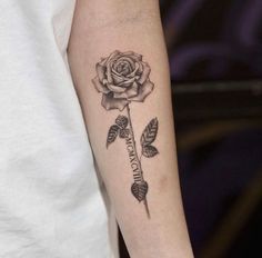 a black and white rose tattoo on the left arm, with two feathers in it