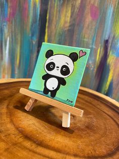 a small wooden easel with a painting of a panda bear on it