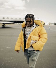 a woman in a yellow jacket is walking towards an airplane on the tarmac with her hands in her pockets