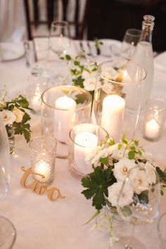 the table is set with candles, flowers and glass vases for centerpieces