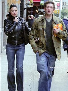 the man and woman are walking down the sidewalk together, holding hotdogs in their hands