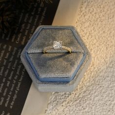 an engagement ring sitting on top of a blue velvet box next to a white wall