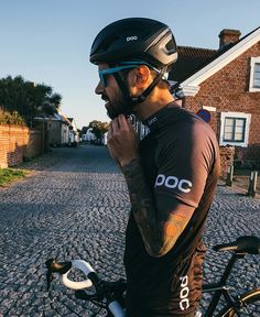 a man standing next to his bike on the street wearing a black t - shirt